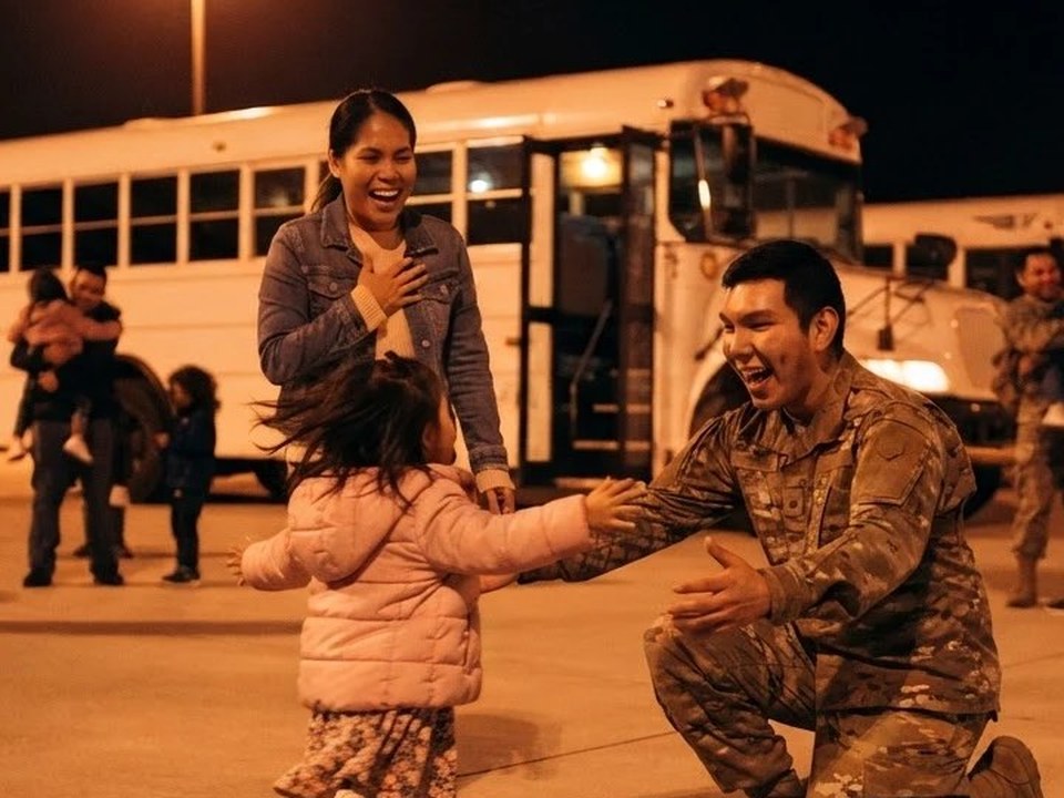 A wife laughing with a hand on her heart while her daughter runs across the concrete toward her father